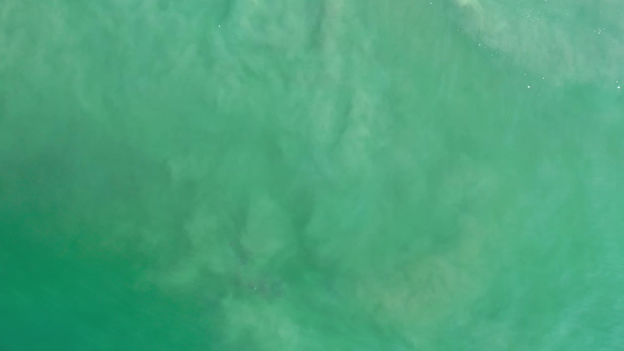 Turquoise ocean surface in Los Cabos, Mexico, seen from above with soft milky streaks and no visible people.