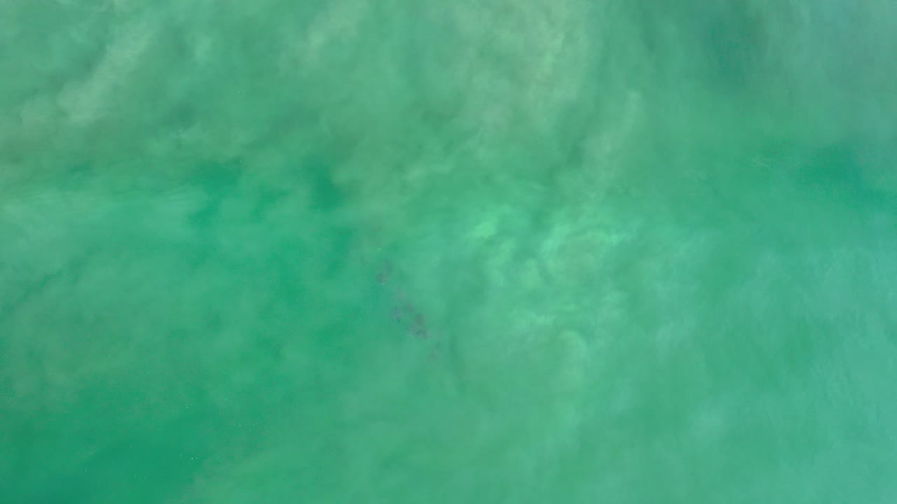 Turquoise ocean water with pale wave texture and a small dark island shape.