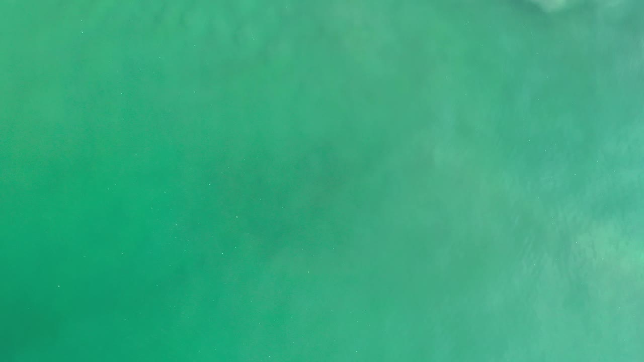Top-down view of green-blue ocean water in Los Cabos, Mexico at the start of the clip, with pale underwater texture near the upper edge and no visible people.
