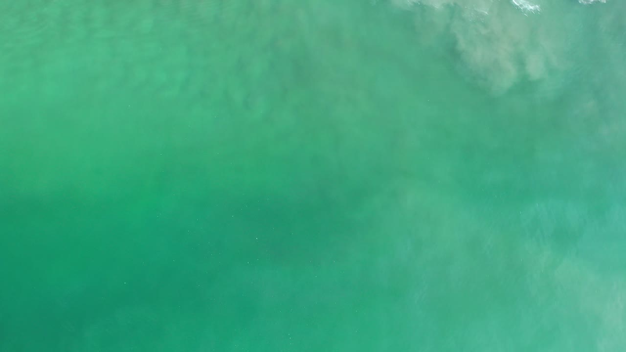 Overhead view of green ocean water in Los Cabos, Mexico, with faint white foam along the upper edge and no visible people.
