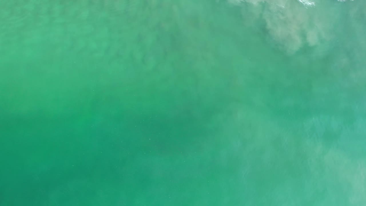 Turquoise ocean surface in Los Cabos, Mexico, with pale underwater swirls, a thin broken foam line near the top, and no visible people.