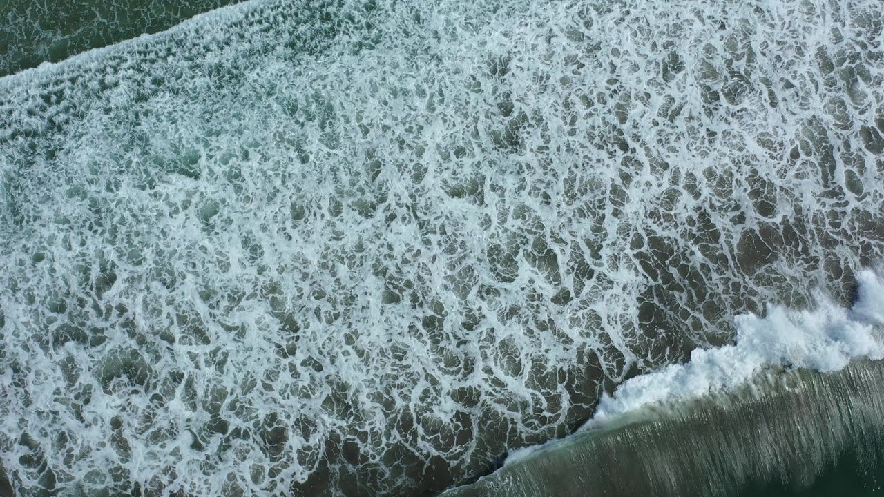 Aerial view of surf foam and a diagonal breaking wave.