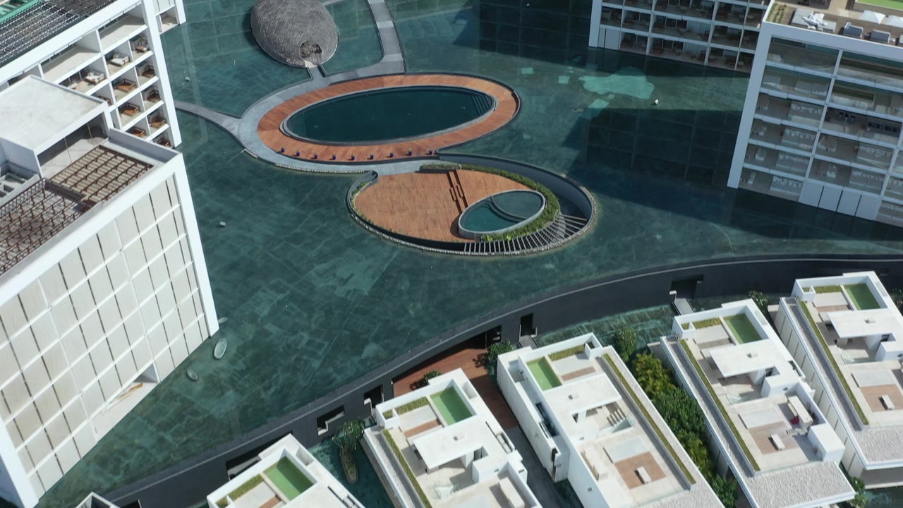 Overhead aerial view of white buildings, paved courtyards, and oval water features.
