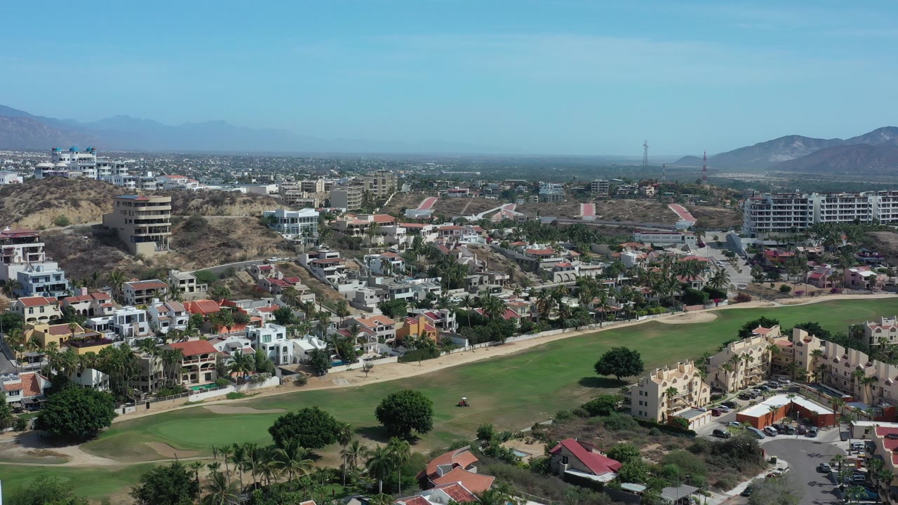 Aerial view of homes, golf course grass, roads, and distant mountains.