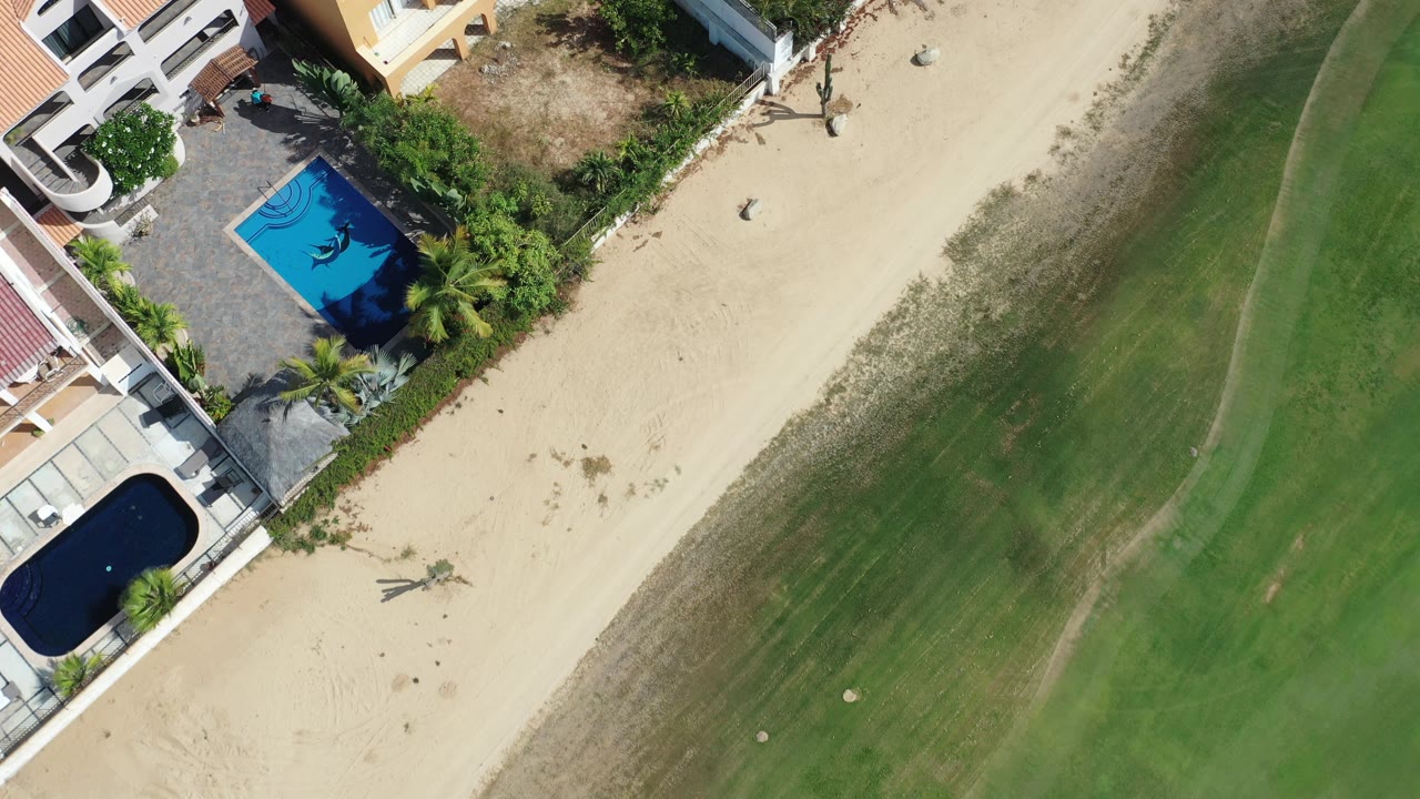 Aerial view of beachfront buildings, sand, and shallow ocean.