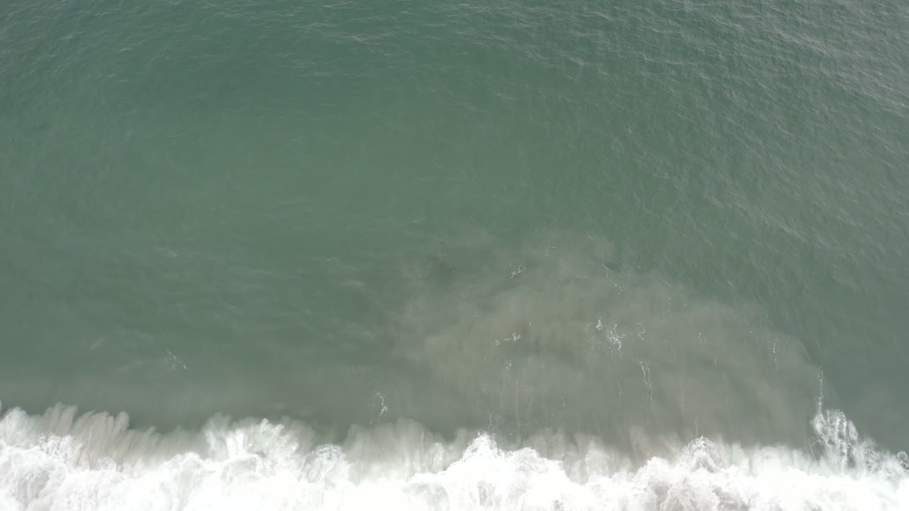 Aerial Los Cabos ocean frame with muted green-blue water, a wider strip of broken white foam at the bottom, and no visible people.
