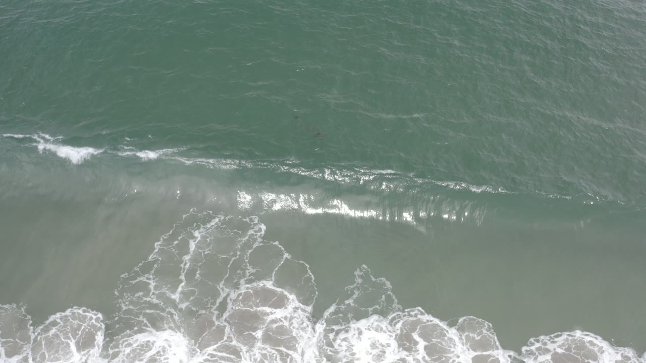 Overhead view of green-blue tidal water and white surf along the lower edge in Los Cabos, Mexico, with no visible people.
