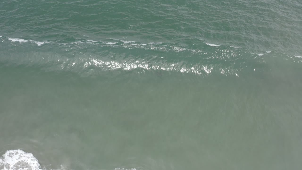 Overhead view of blue green surf breaking near sandy shallows in Los Cabos, Mexico, with no visible people.