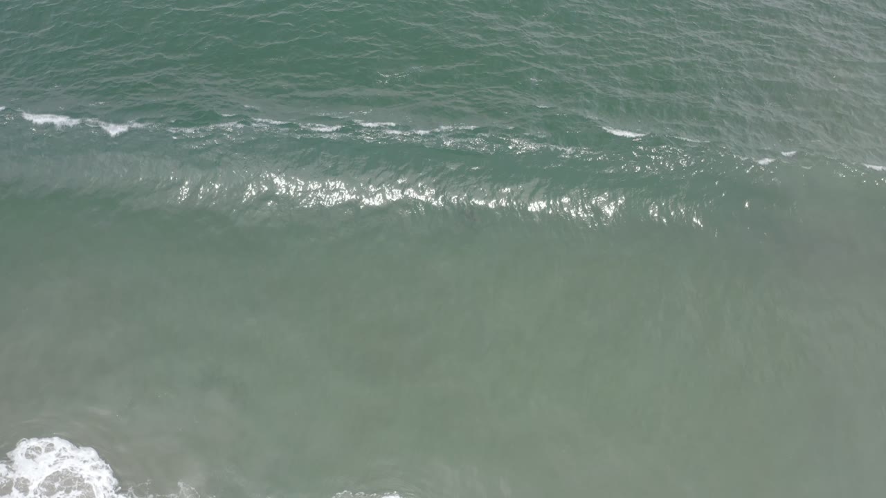 A straight-down frame of rippled green ocean water in Los Cabos, Mexico, with a thin white breaker line and no visible people.