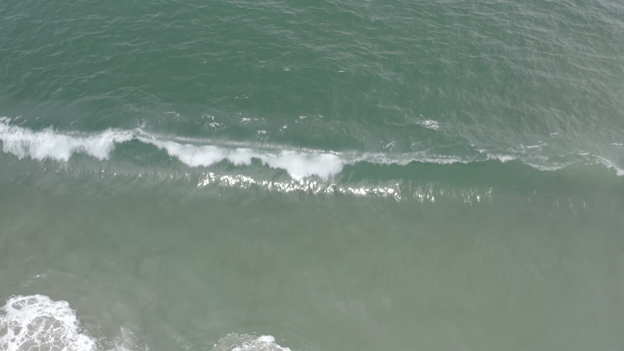 White surf line crossing blue green water from an overhead angle.