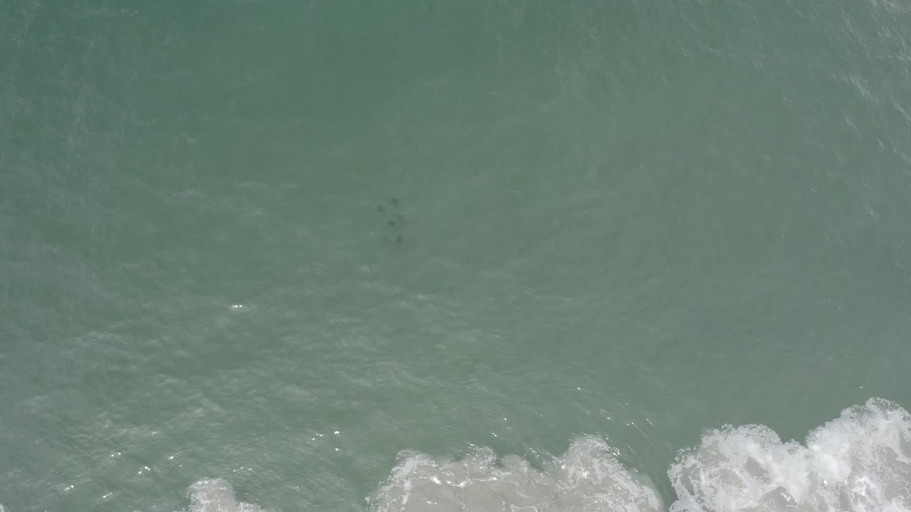 Aerial view of Los Cabos ocean water with a band of white foam pushing farther into the lower frame and no visible people.