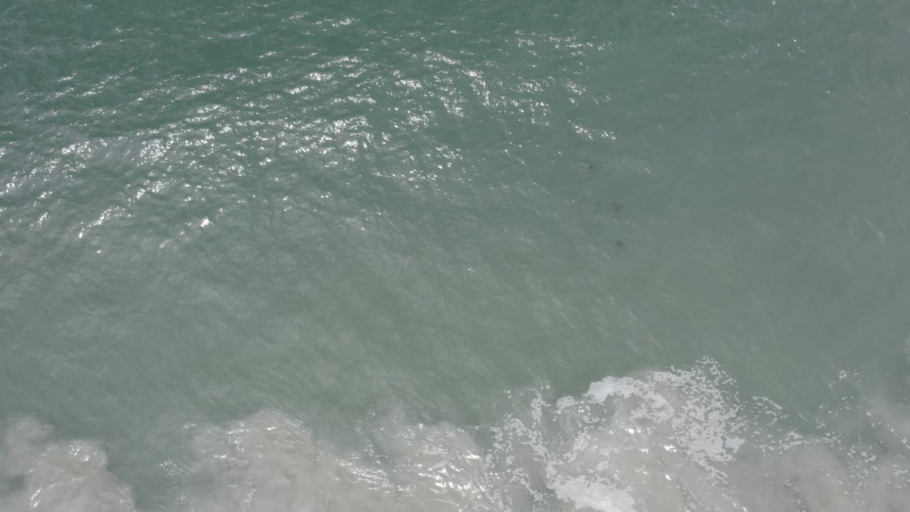 Overhead water view with brighter sun reflection and foamy surf below.