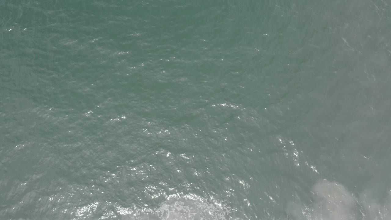 Clear ocean surface with ripples and faint dark shapes under water.