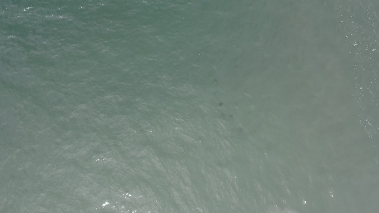 Aerial view of Los Cabos ocean water with light ripples, gray-green color, and small highlights near the lower edge, with no visible people.