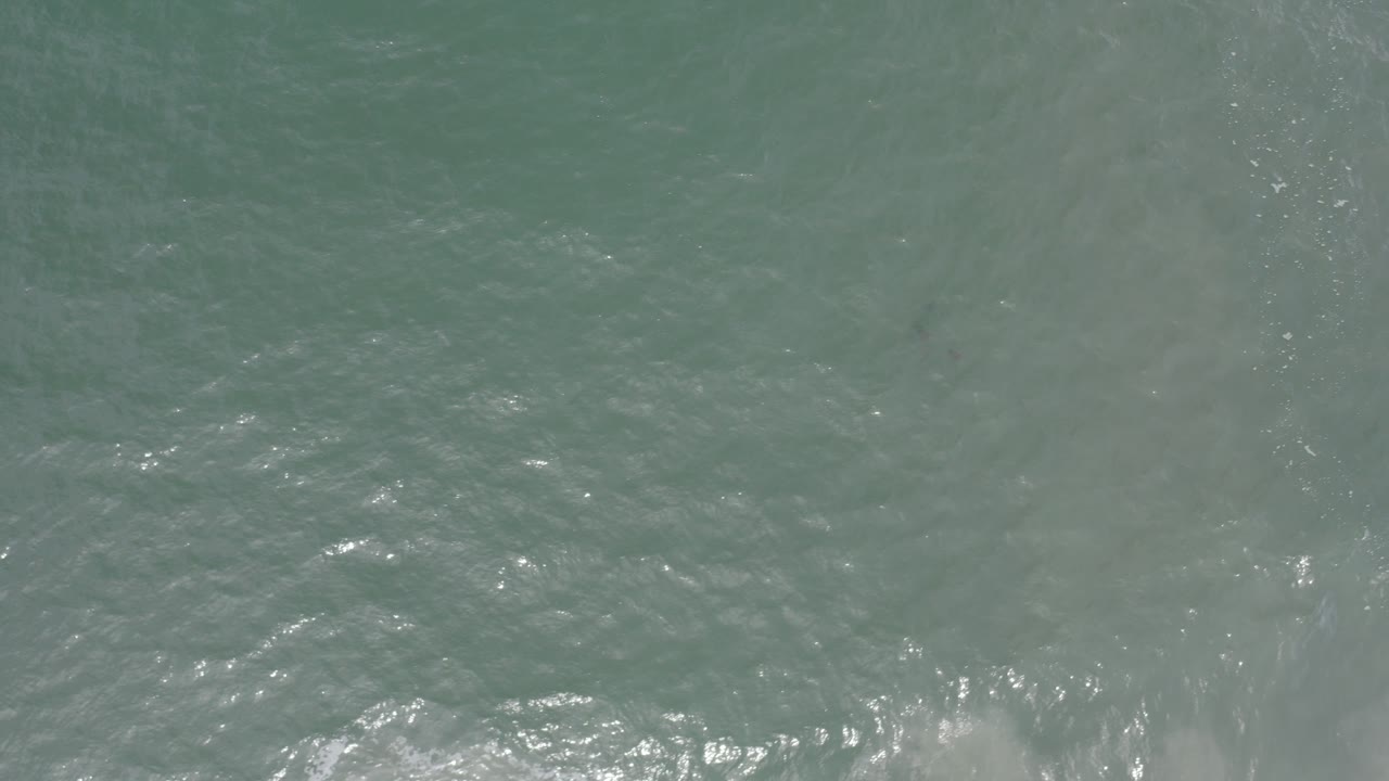 Overhead view of gray-green sea water in Los Cabos, Mexico, with soft foam streaks near the lower edge and no visible people.
