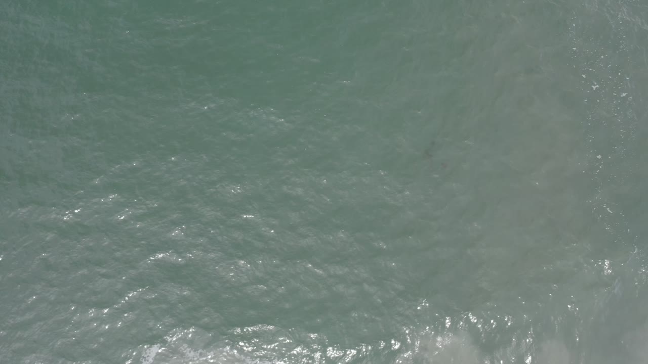 Gray-green water fills the frame in Los Cabos, Mexico, with brighter broken foam gathering along the lower portion and no visible people.