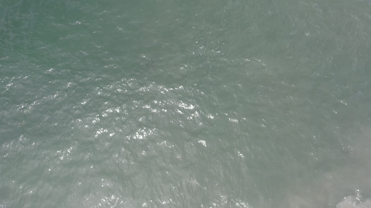 Overhead view of gray green ocean water in Los Cabos, Mexico, with a faint band of white foam entering along the lower edge and no visible people.