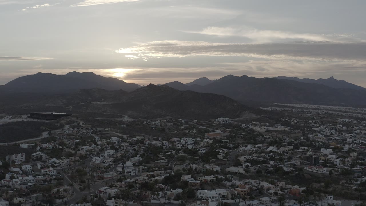 Residential area and desert hills seen from above near a bright sunset sky.