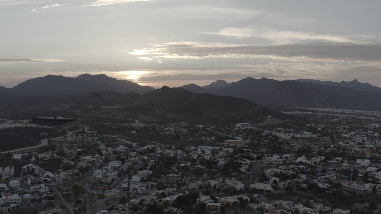 Aerial town view below dark hills at sunset