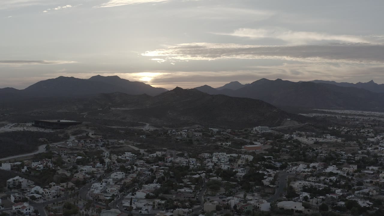 Aerial view of town below dark hills at sunset