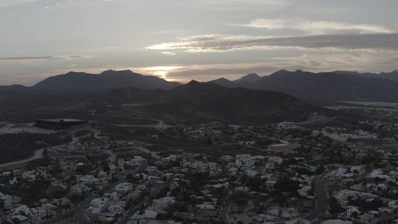 Wide aerial view of town, hills, mountains, and cloudy sunset sky.