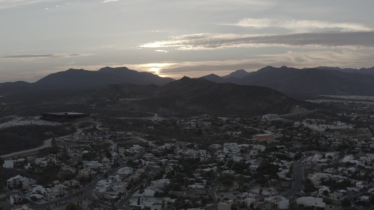 Aerial view of a town below dark hills at sunset.