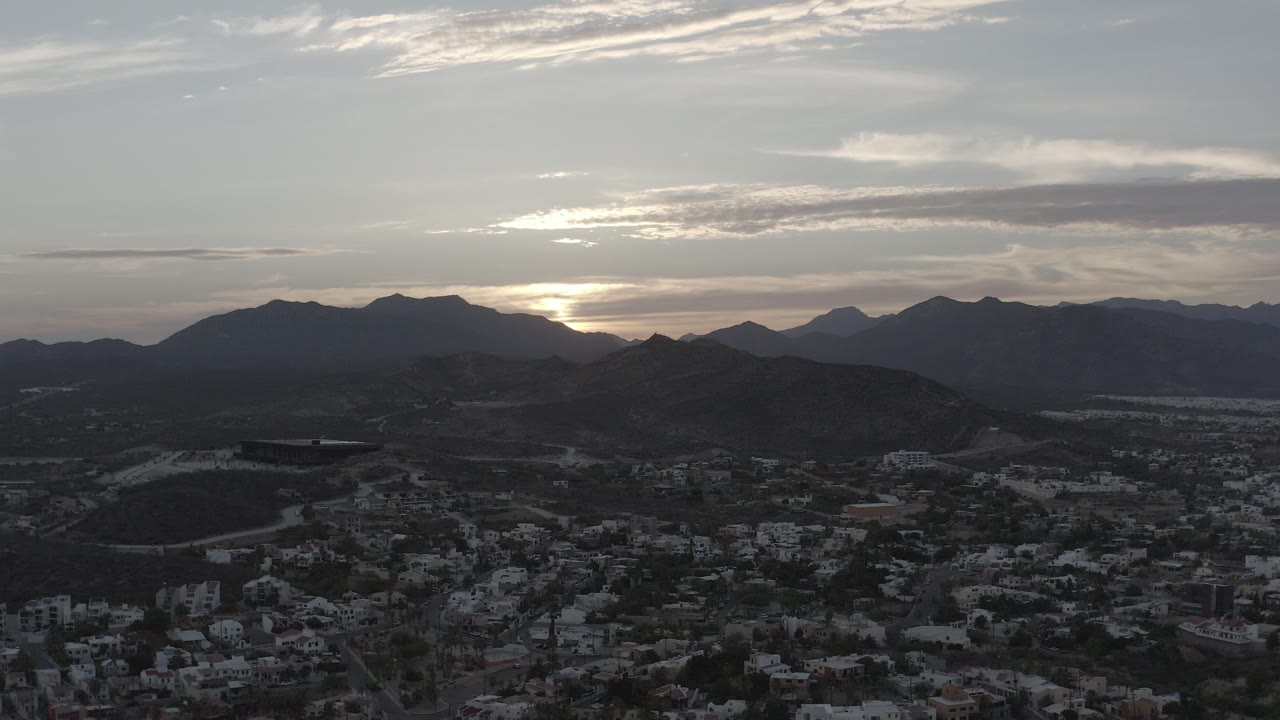 Aerial view of a town below dark hills at dusk.