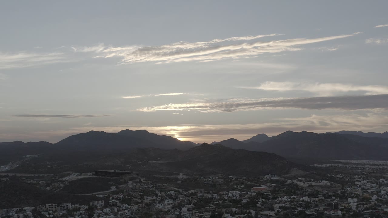 Wide view of mountains silhouetted under a cloudy sunset sky.