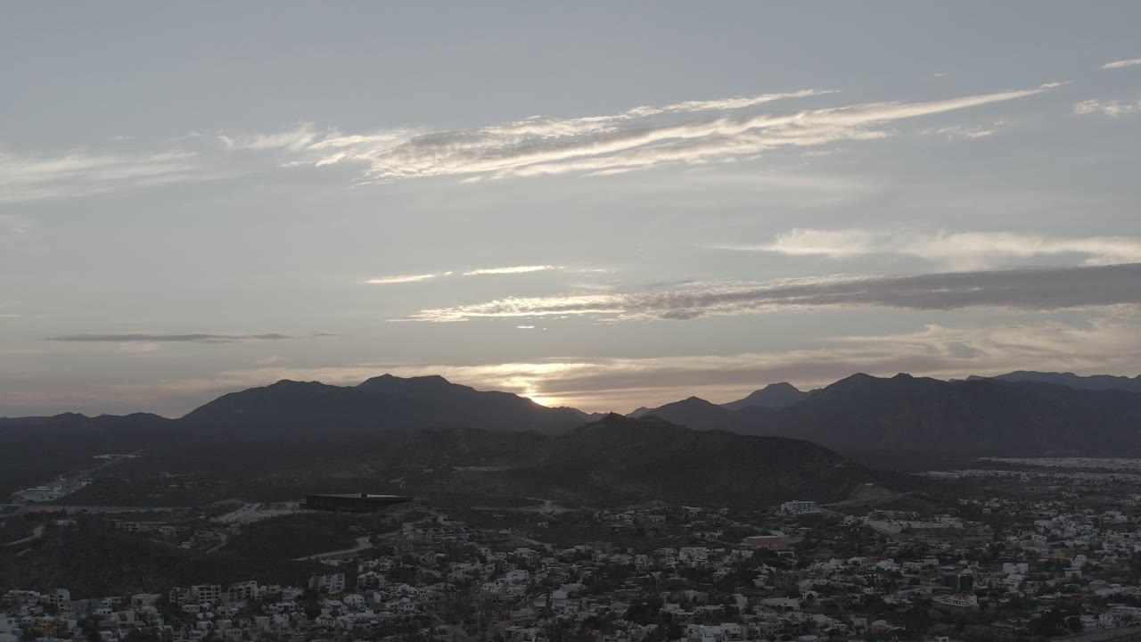 Opening frame of Los Cabos, Mexico, with dark mountain silhouettes, a low city foreground, pale light near the horizon, and no visible people.