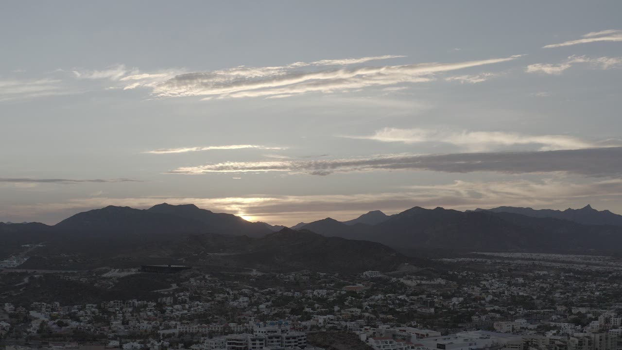 Sunset behind dark mountain ridges above a city foreground.