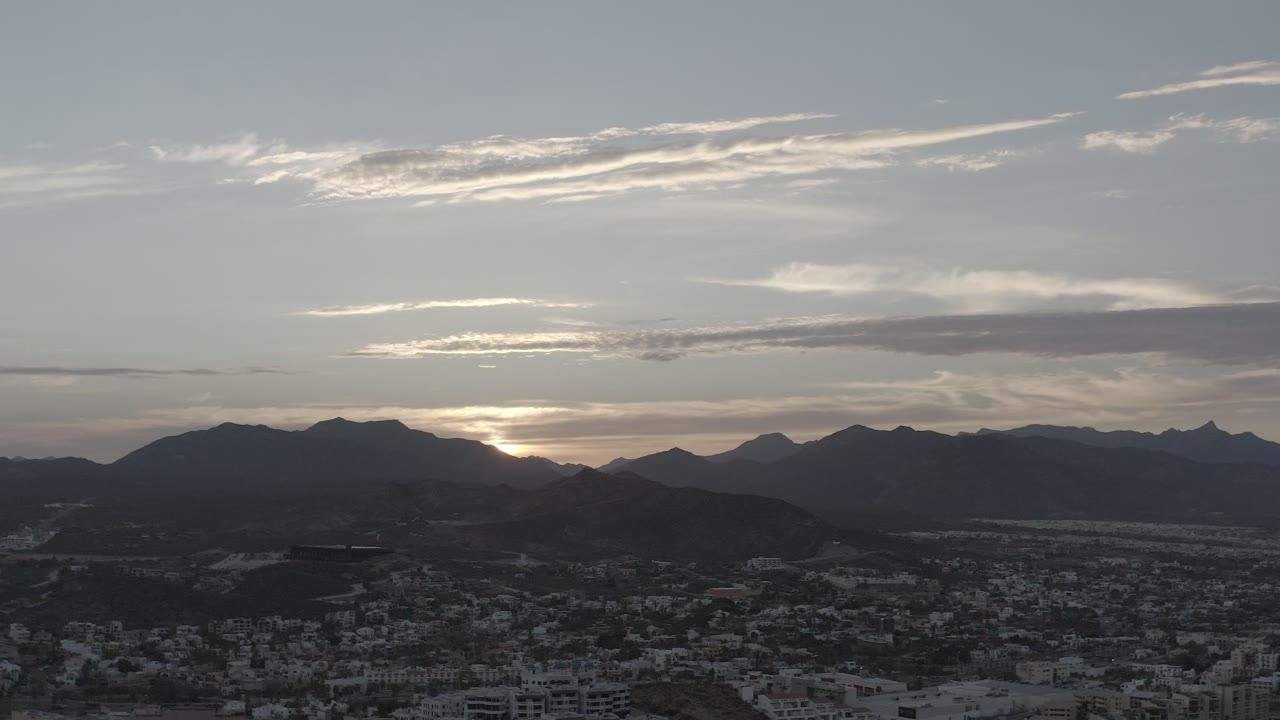 Second frame of the Los Cabos sunset view, with the bright sun partly hidden behind the left mountain ridge and no visible people.