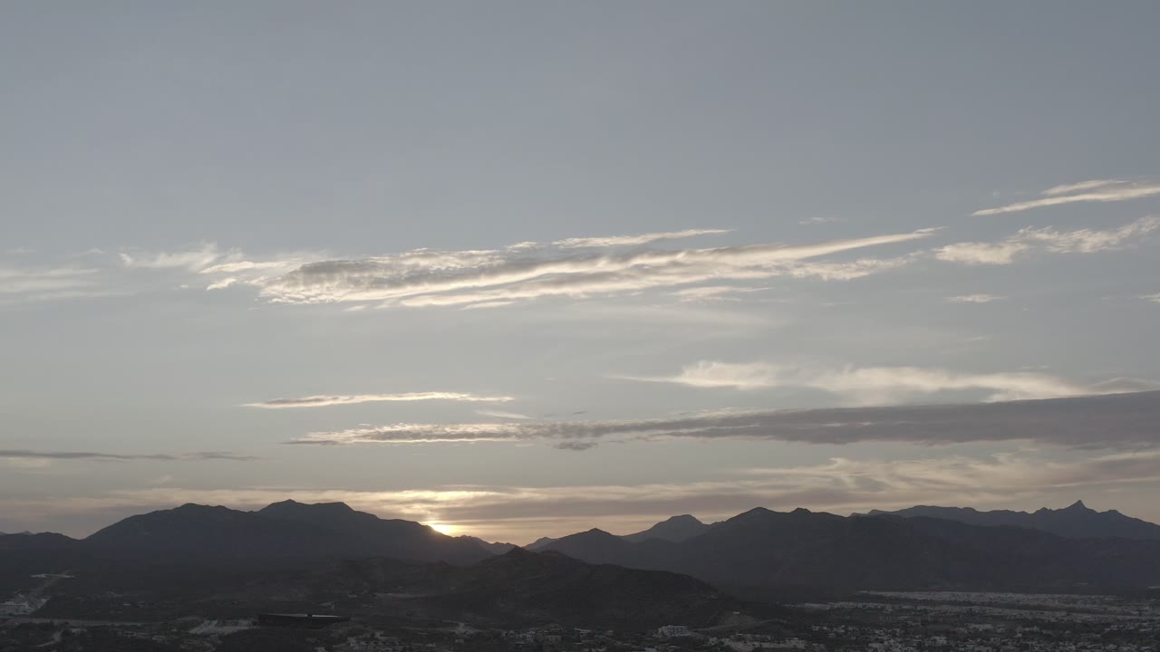 Streaked clouds above a dark mountain horizon at sunset.
