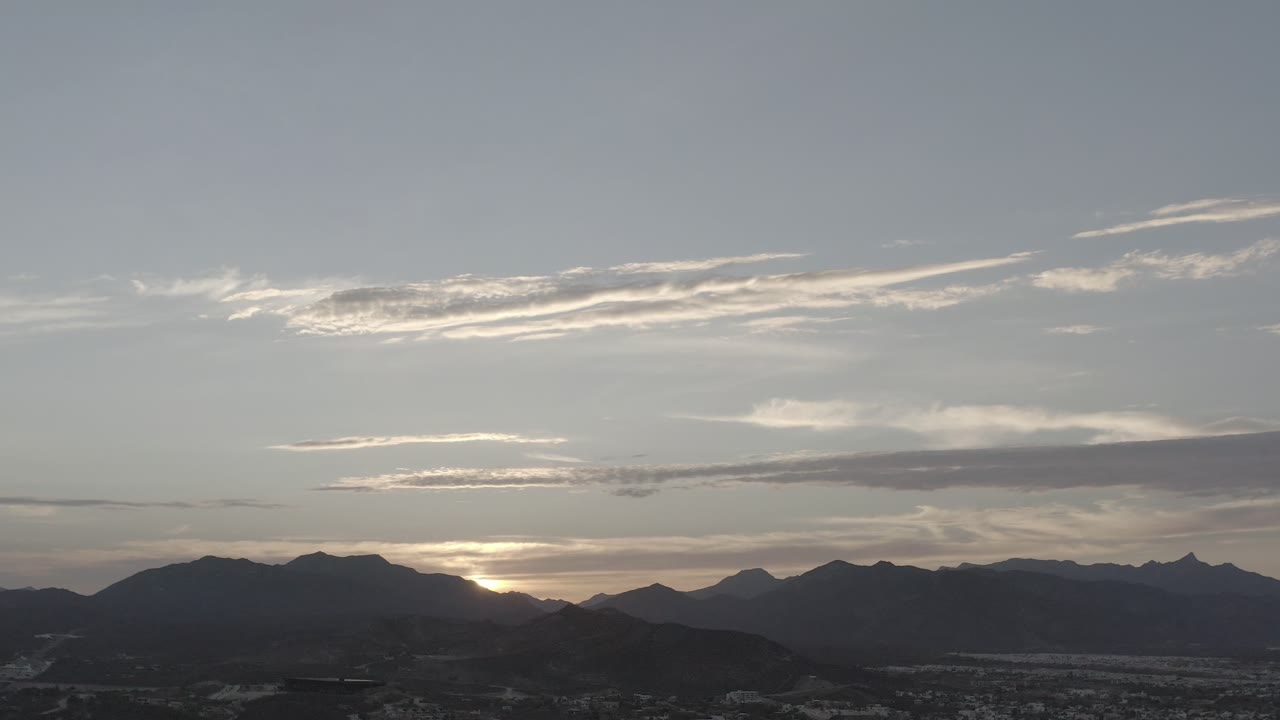 Los Cabos, Mexico mountain skyline with the sunset glow partly hidden behind the ridgeline, long gray cloud streaks, and no visible people.