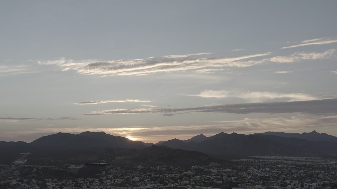 Wide aerial view of clouds over dark hills and city
