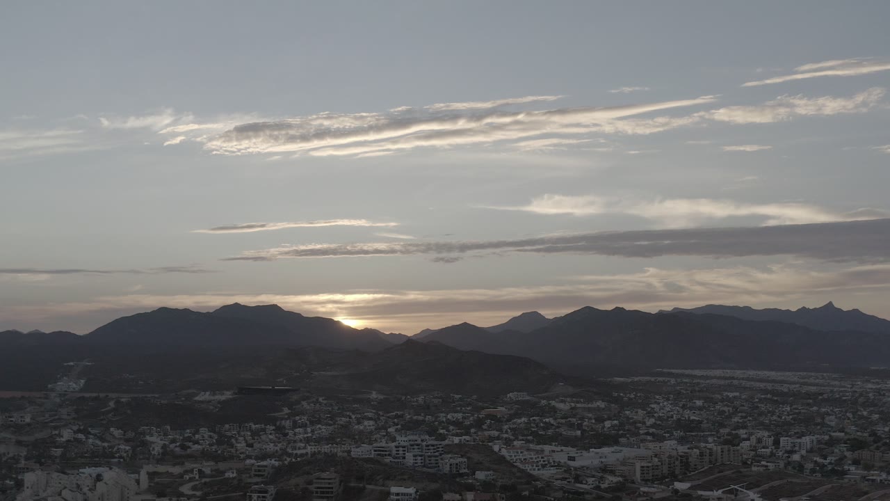 Sunset glow behind mountains over a shadowed town.