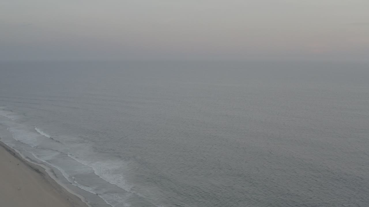 Overcast aerial coastline with small waves reaching the sand.