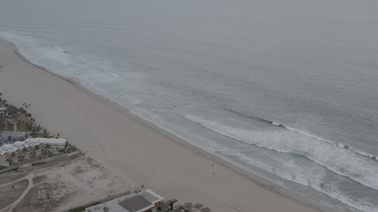 Aerial view of an overcast beach with waves and beachfront buildings.