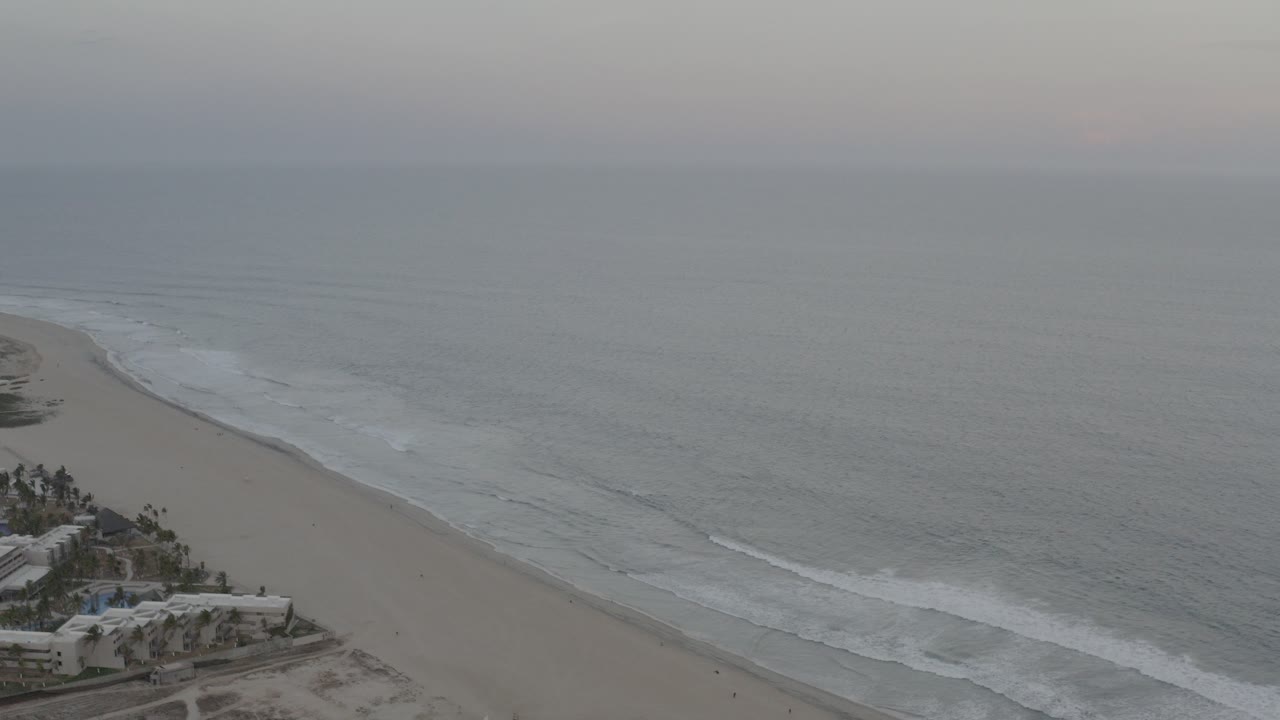 Overcast coastline with waves rolling onto a sandy beach.