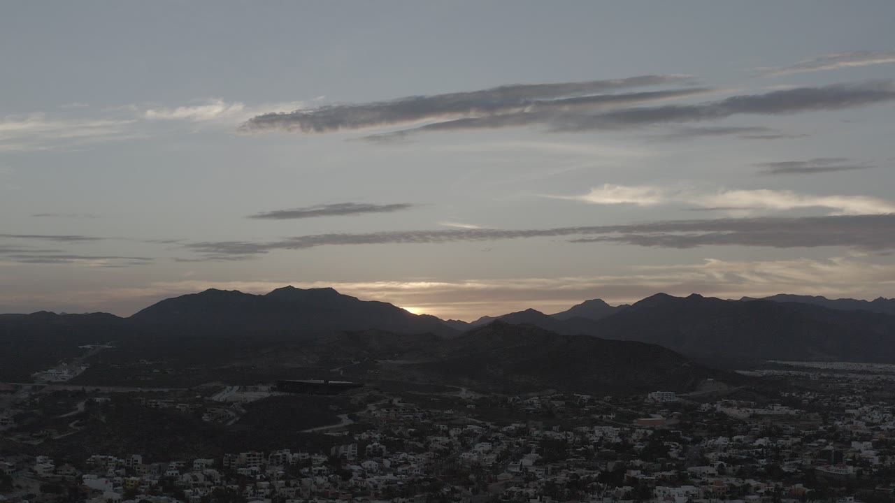 Wide dusk view of mountains, town, clouds, and sunset glow.