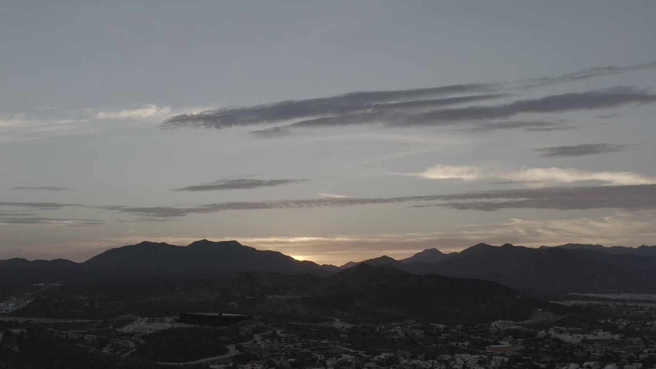 Twilight sky over dark mountain ridges and distant town buildings.