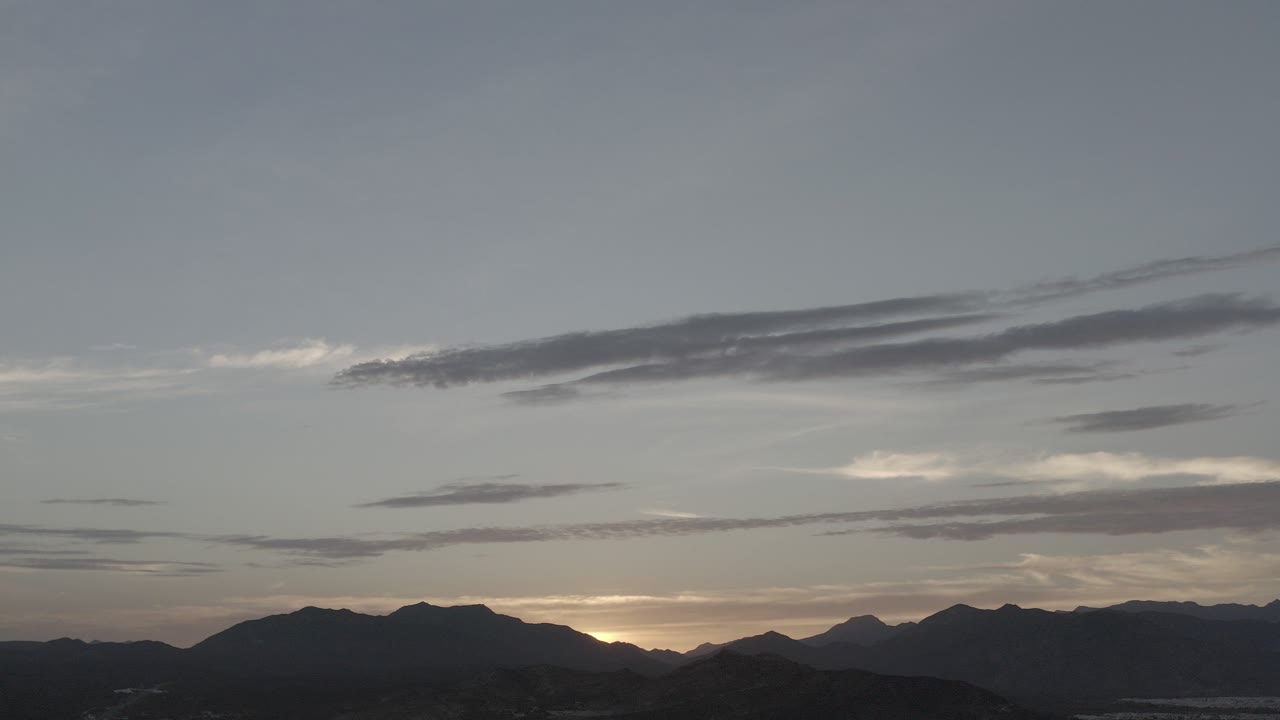 Mountain silhouettes under a dim sunset sky with layered clouds.
