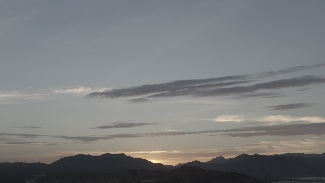 At the start of the Los Cabos clip, long gray cloud bands stretch above silhouetted hills, with a small warm glow on the horizon and no visible people.