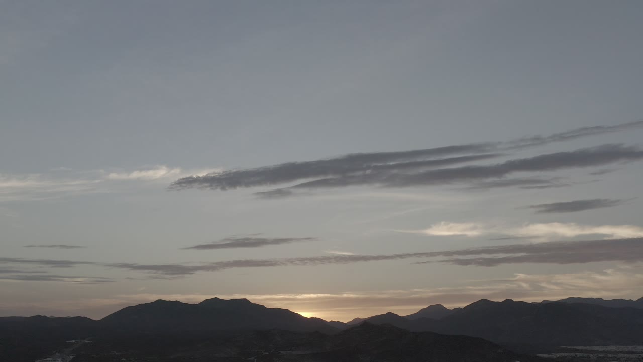 Sunset glow behind layered hills under thin clouds.