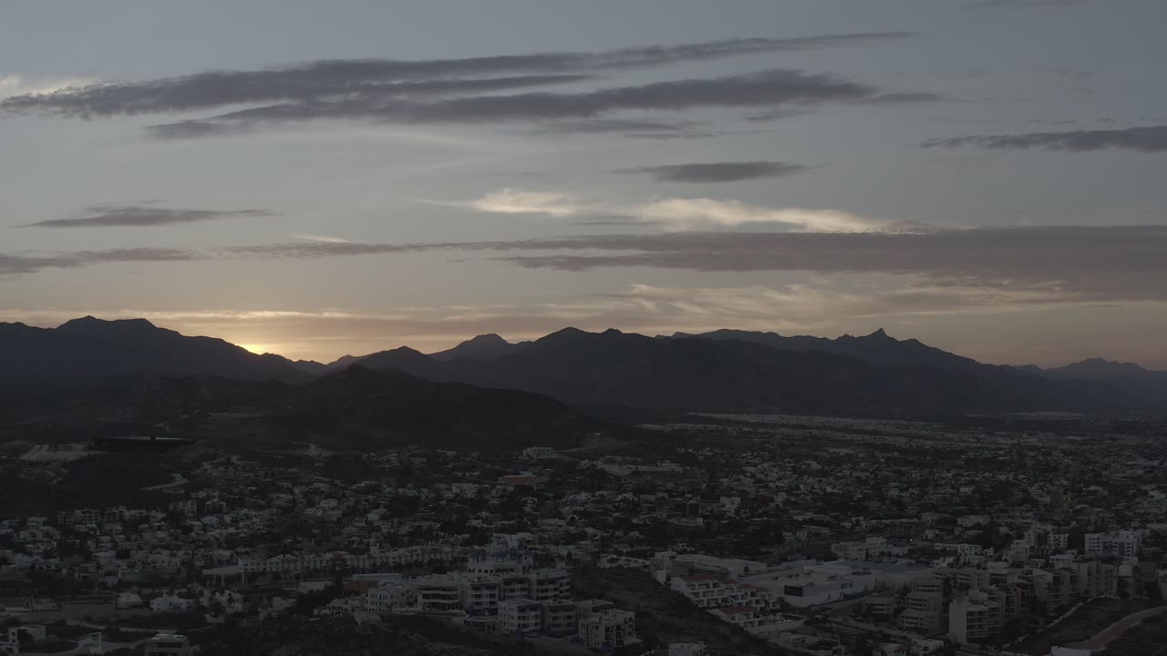 Clouded dawn sky over mountain ridges and a valley community.