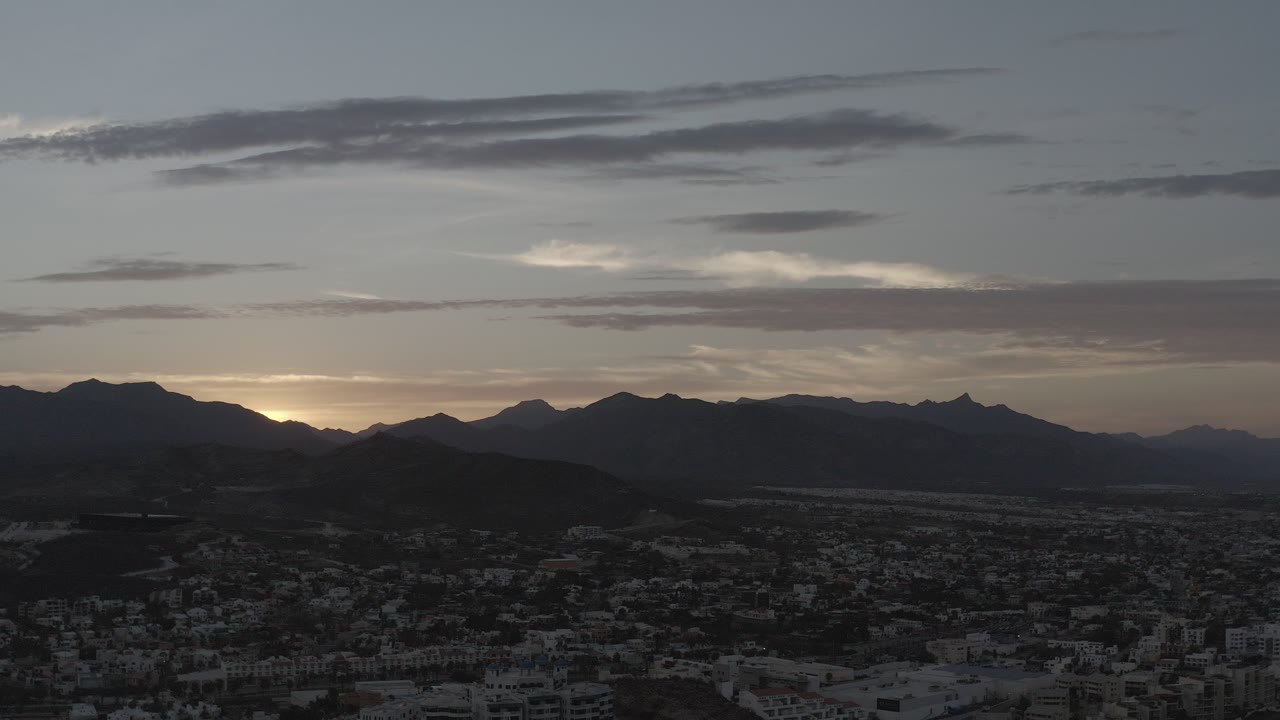 Dusk aerial over a dark city below a mountain horizon.