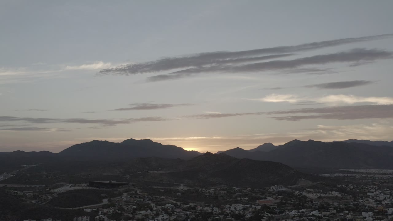 Wide dusk view over a town, hills, and mountain silhouettes.