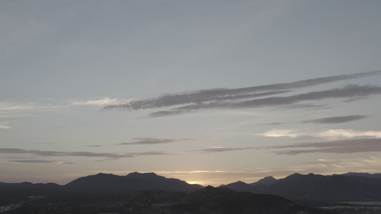 Opening frame of Los Cabos, Mexico mountains in dark silhouette beneath a pale gray-blue sunrise sky, with no visible people.