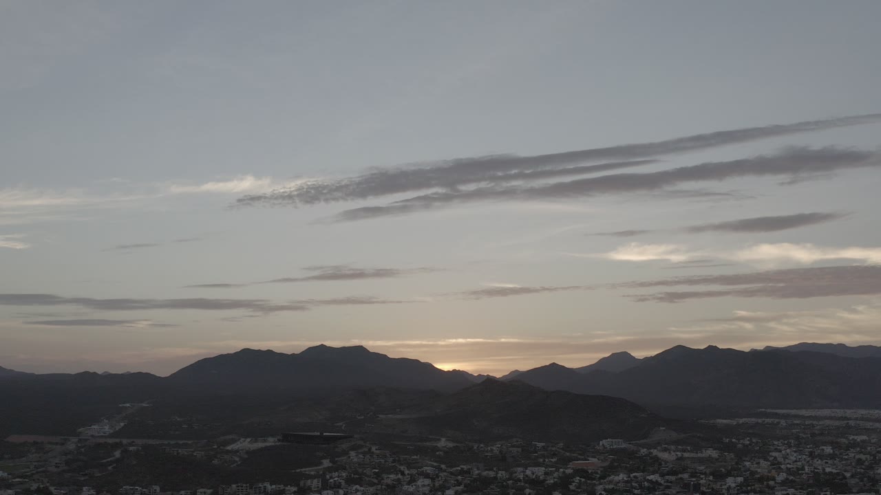Wide aerial cityscape below dark mountain ridges at dusk.