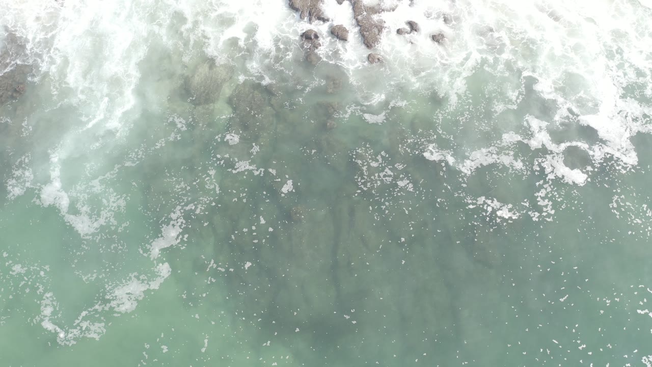 Overhead turquoise ocean water with white surf and rocks near the top edge.