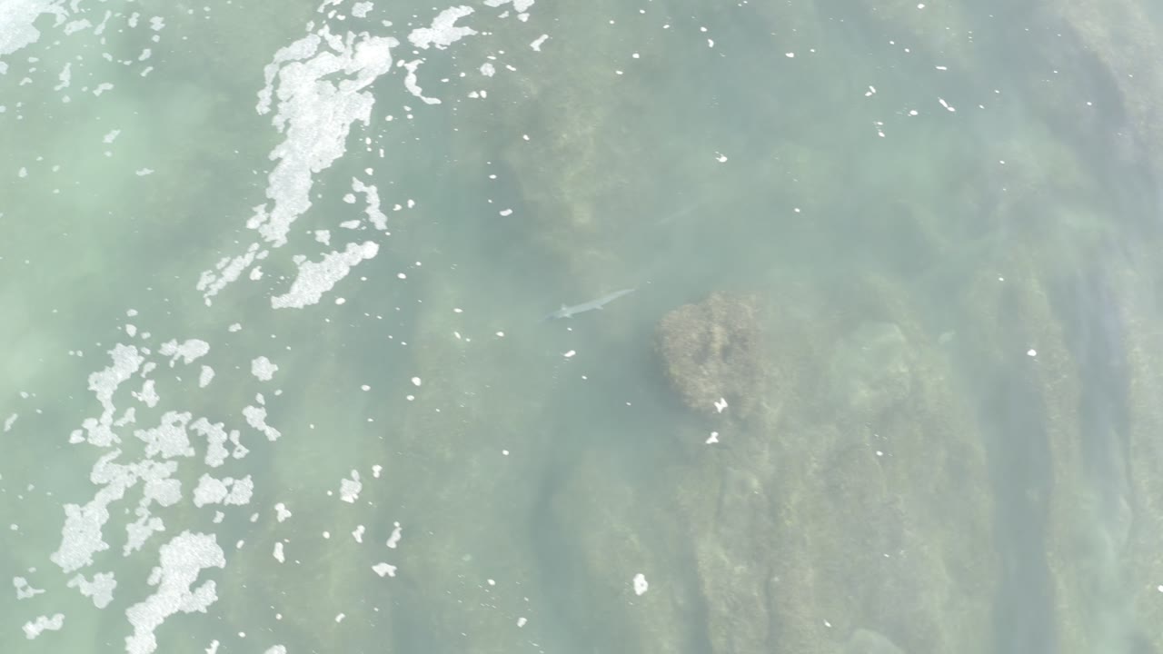 Foam streaks over shallow blue-green water and rocks